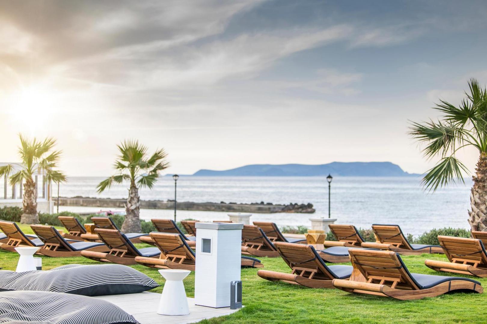 Atpūtas zona ar koka sauļošanās krēsliem un sēžammaisiem Insula Alba Resort & Spa zālājā pie jūras Krētā