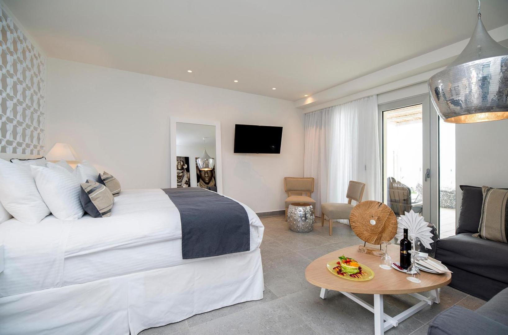Insula Alba Resort & Spa moderns viesnīcas numurs ar baltu gultu, dizaina mēbelēm, spoguli un izeju uz terasi.