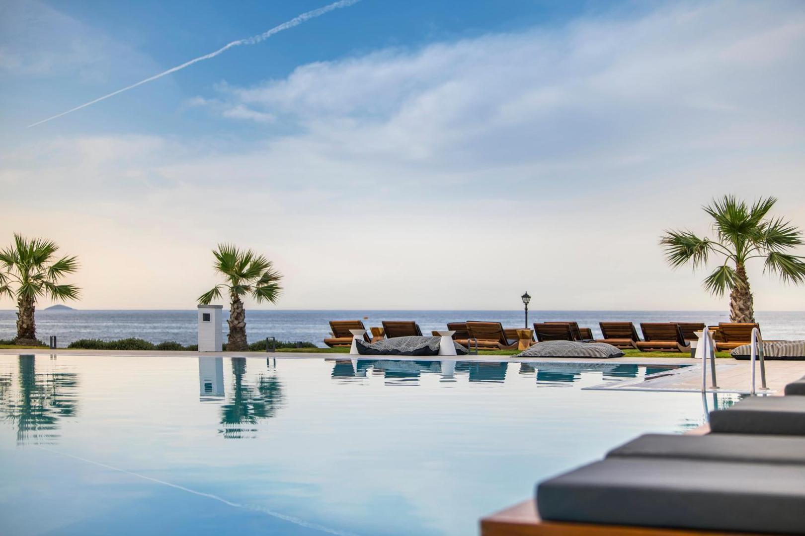 Insula Alba Resort & Spa bezgalības malas baseins ar skatu uz Vidusjūru — sauļošanās krēsli, palmas un gaišas debesis Krētā