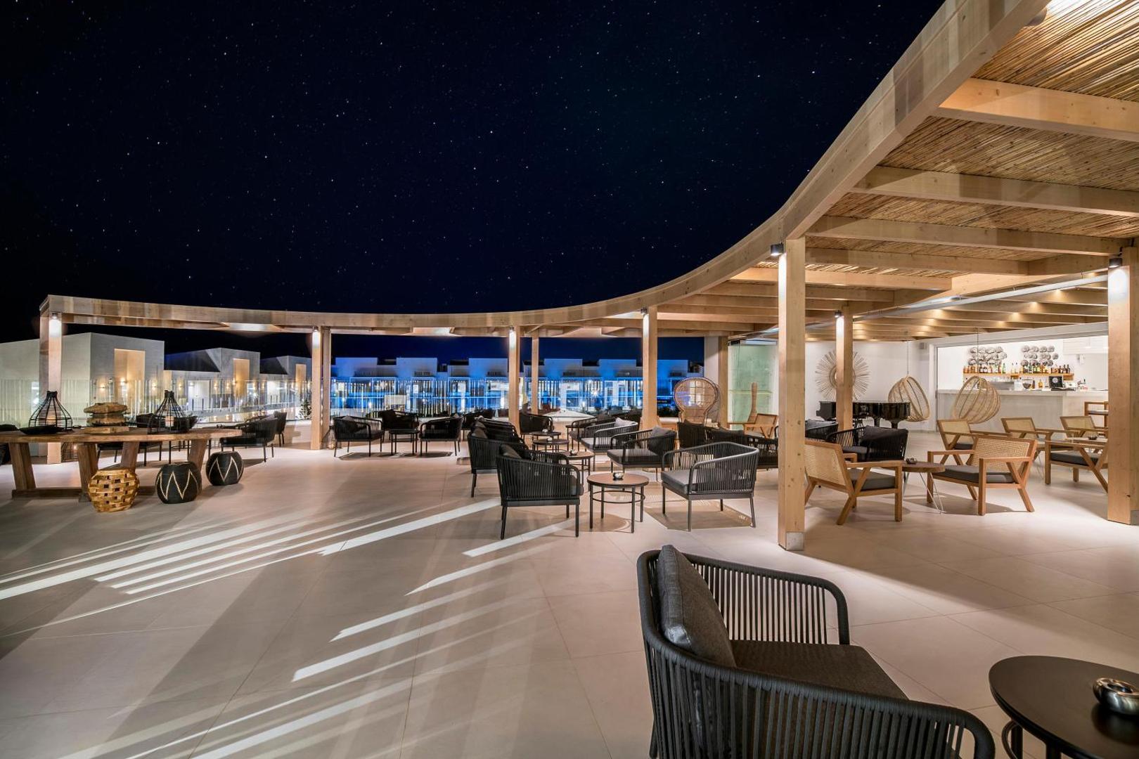 Insula Alba Resort & Spa modernā jumta terase naktī Hersonisā, Krētā — eleganti atpūtas krēsli zem koka nojumes ar skatu uz zvaigžņotām debesīm