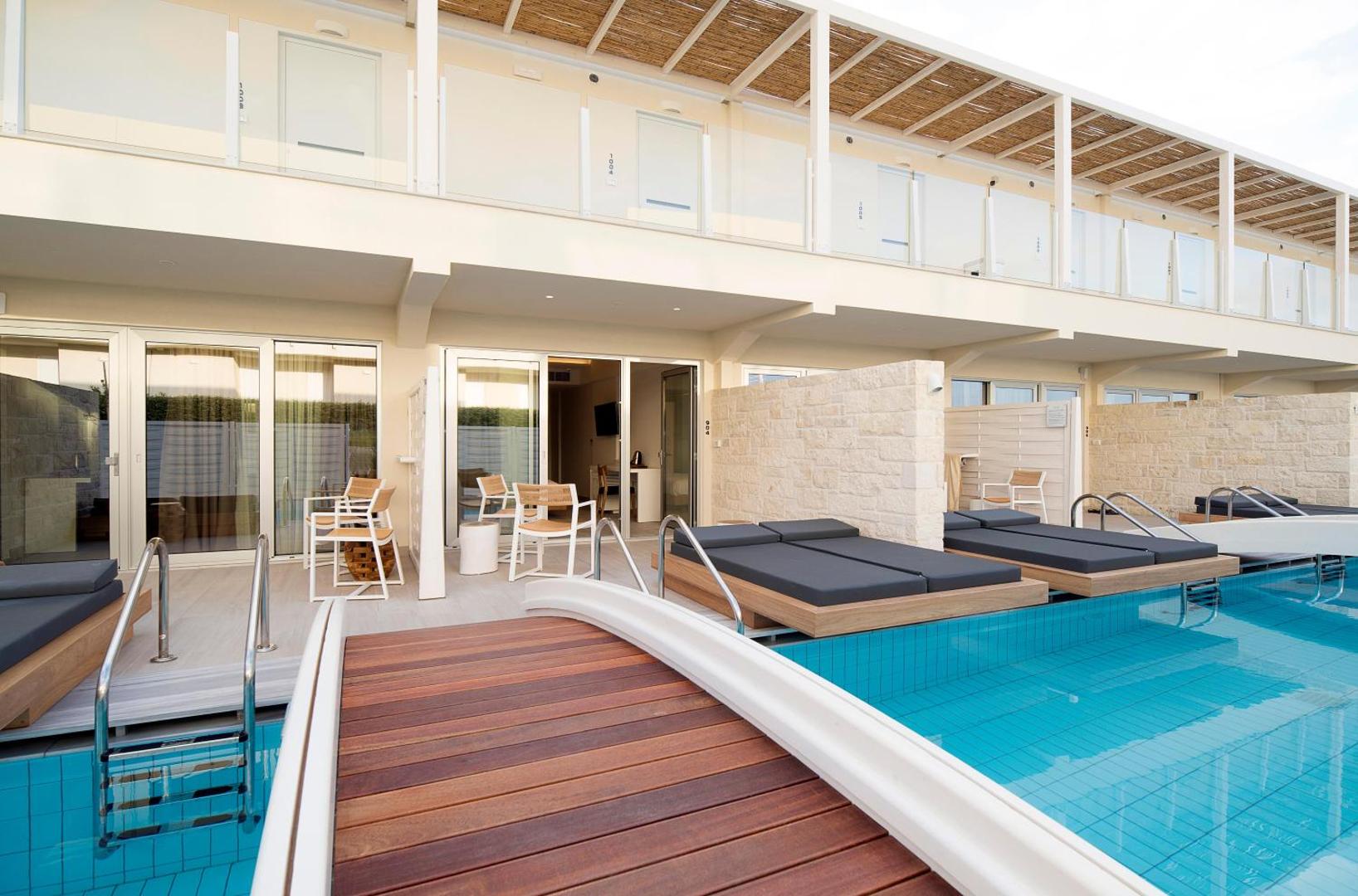 Insula Alba Resort & Spa numuri ar tiešu piekļuvi baseinam Krētā — terase ar sauļošanās krēsliem un koka tiltiņu pāri ūdenim