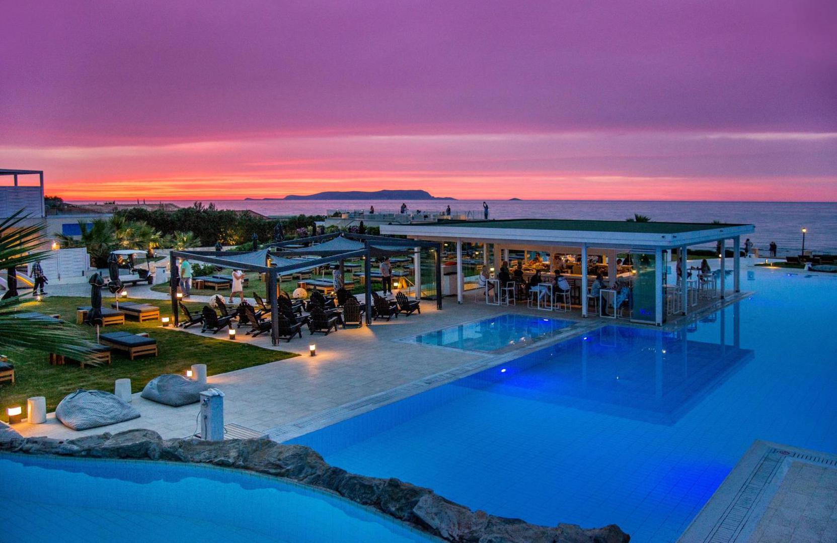 Insula Alba Resort & Spa āra baseins un bārs pie jūras saulrietā — plaša atpūtas zona ar sēžammaisiem un galdiņiem Krētā