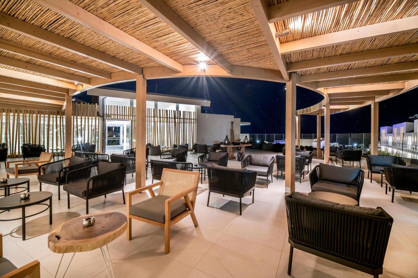 Viesnīcas Insula Alba Resort & Spa atpūtas zona ar dizaina mēbelēm un koka apdari naksnīgā apgaismojumā Krētas piekrastē