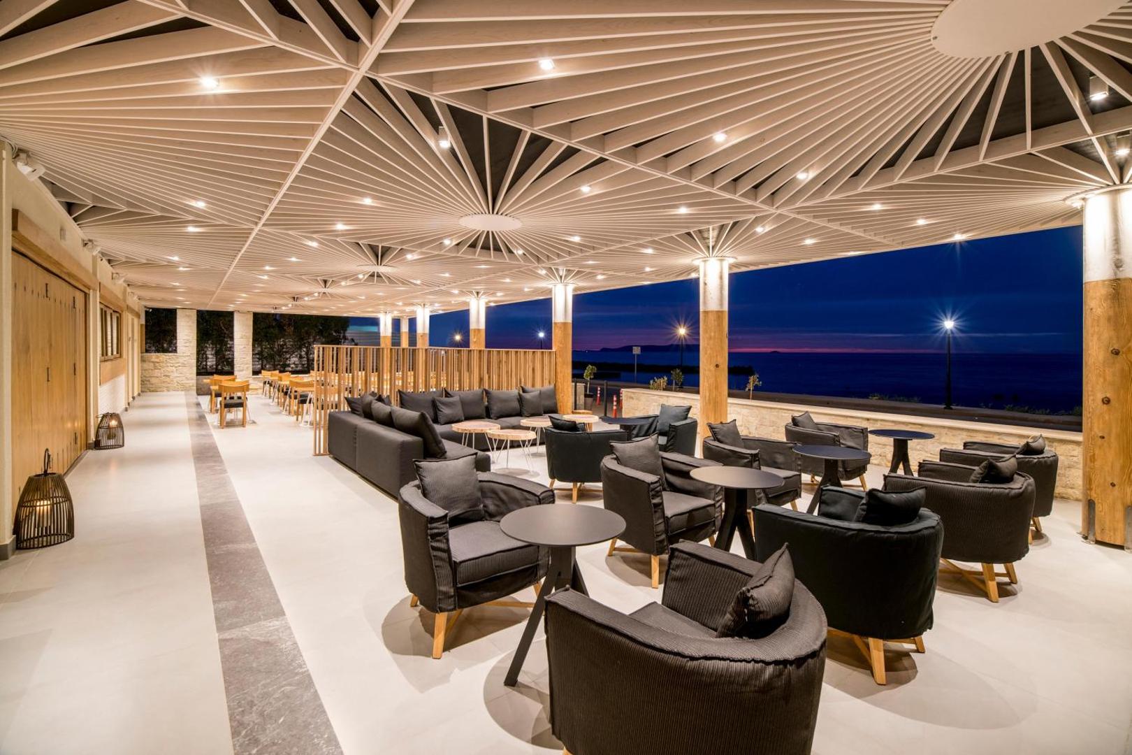 Insula Alba Resort & Spa āra terase ar moderniem atpūtas krēsliem un skatu uz jūru saulrieta laikā Krētas piekrastē