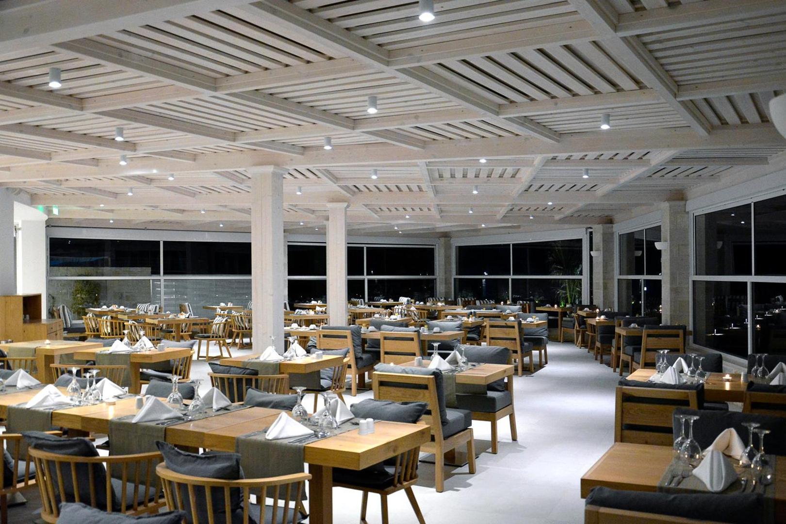 Insula Alba Resort & Spa galvenais restorāns ar koka griestu apdari un elegantiem galdiem vakariņu laikā Analipsi ciematā, Krētā