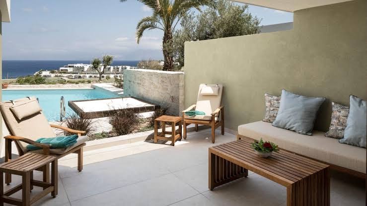 Porto Elounda Golf & Spa Resort numura terase ar dīvānu, koka galdiņu un privātu baseinu piekrastes fonā