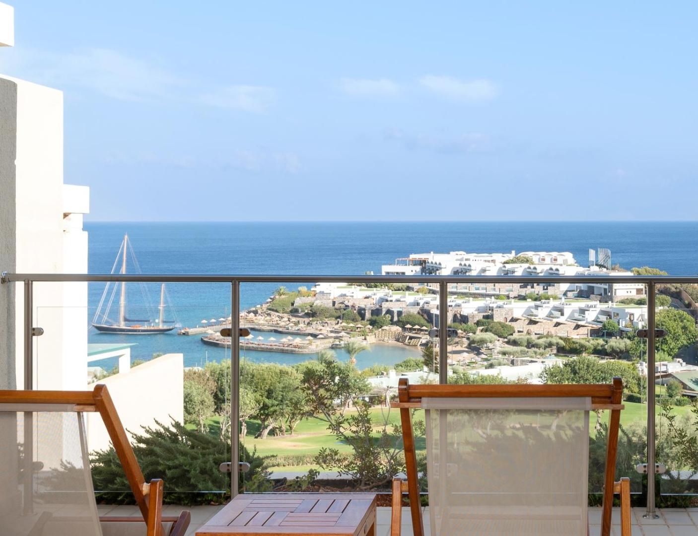 Skats no Porto Elounda Golf & Spa Resort balkona uz piekrasti, jahtu un kūrorta teritoriju saulainā dienā Elundā