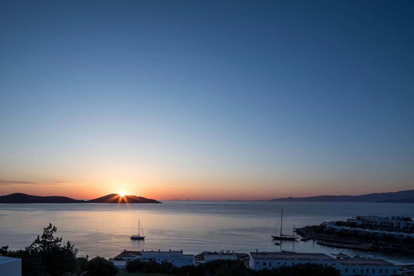 Saulriets virs kalniem un jūras Porto Elounda Golf & Spa Resort kūrortā ar jahtām līcī vakarā