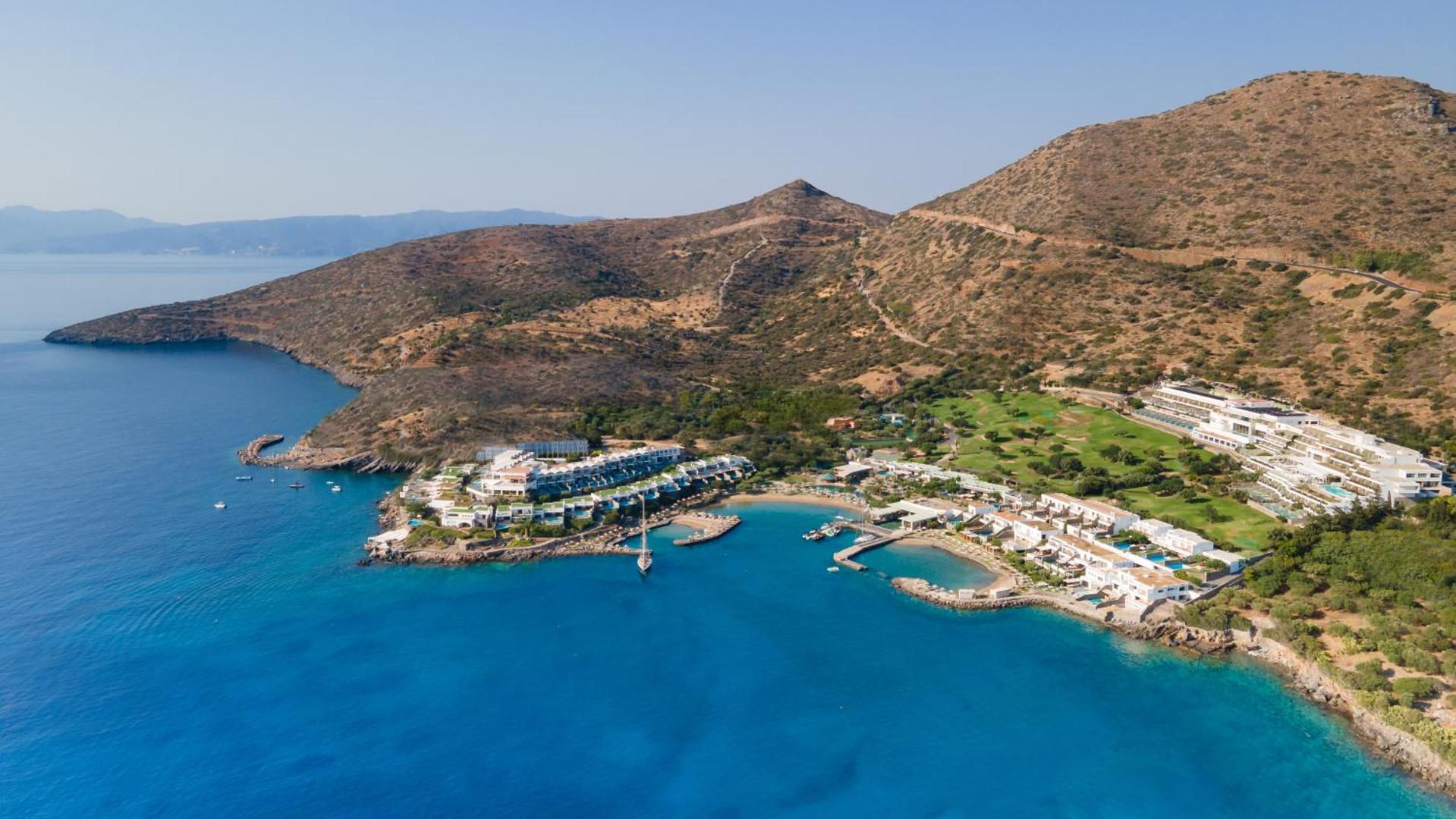 Porto Elounda Golf & Spa Resort panorāmas skats no augšas uz kūrortu, privāto līci un apkārtējiem kalniem Krētā