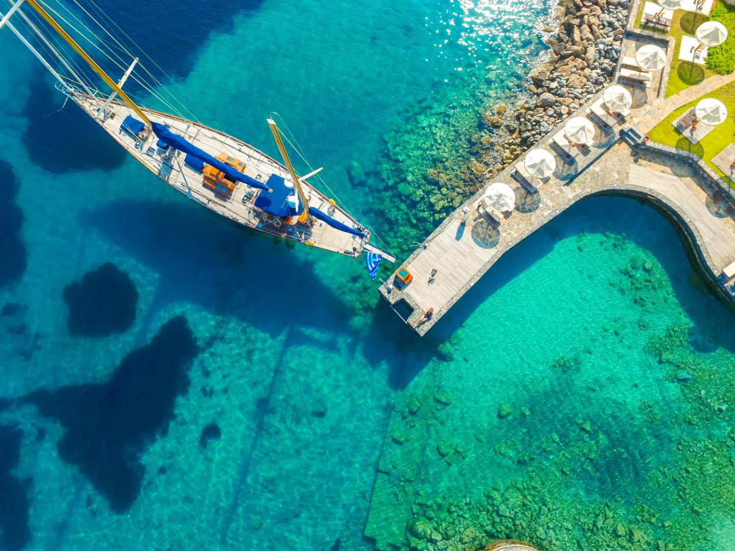 Porto Elounda Golf & Spa Resort koka piestātne un jahta dzidri zilā, caurspīdīgā ūdenī Krētas piekrastē
