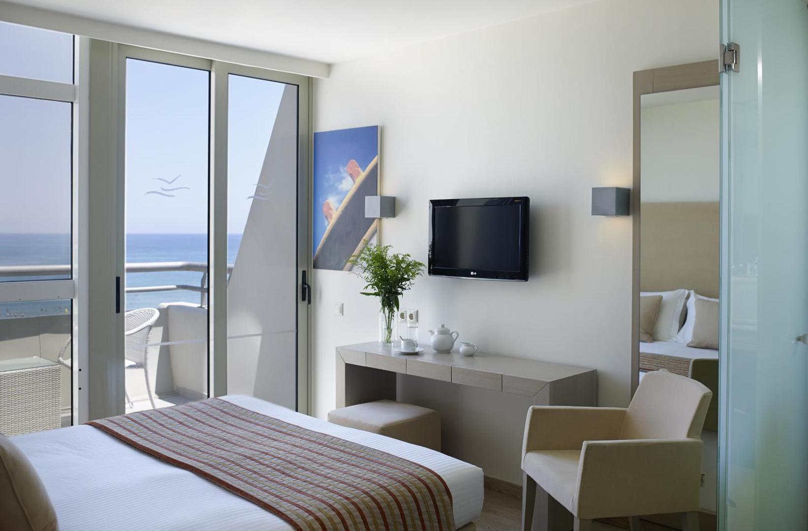 Gaišs Kriti Beach Hotel numurs ar skatu uz jūru — divguļamā gulta, rakstāmgalds, atpūtas krēsls un balkons ar panorāmas skatu