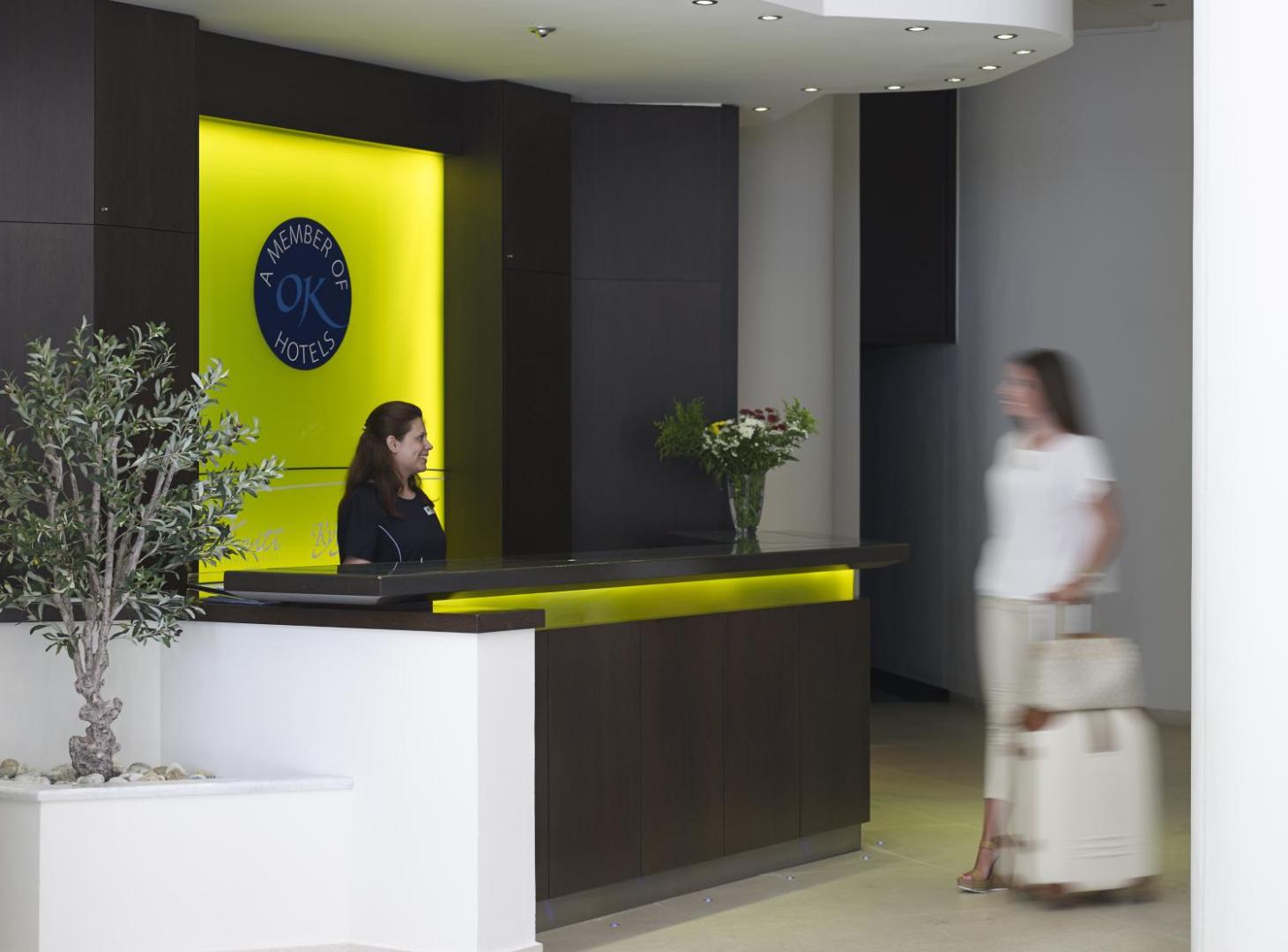 Kriti Beach Hotel reģistratūras lete ar personālu un koši dzeltenu akcenta sienu viesnīcas vestibilā Krētā