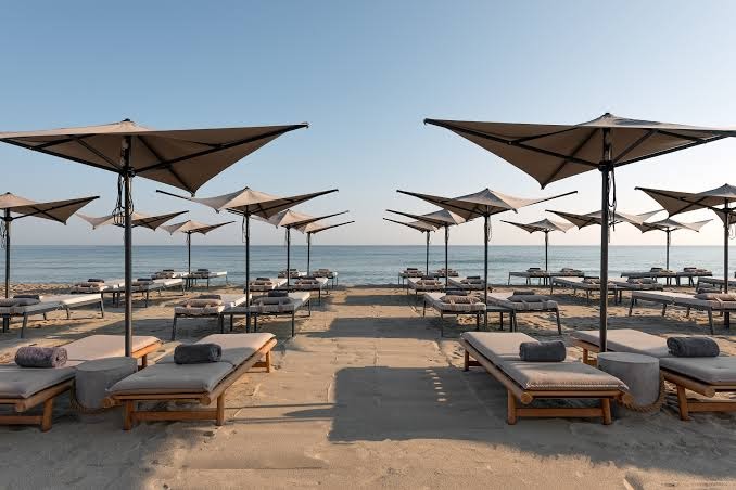 Ikones Seafront Luxury Suites privātā pludmale ar moderniem saulessargiem un koka zviļņiem smiltīs pie dzidrā jūras ūdens