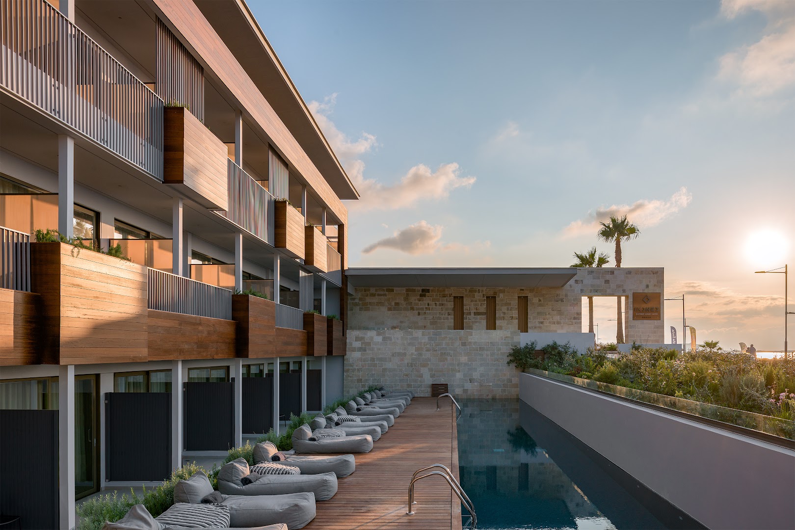 Ikones Seafront Luxury Suites viesnīcas fasāde un āra baseins ar mīkstajiem zviļņiem saulrietā Retimno piekrastē