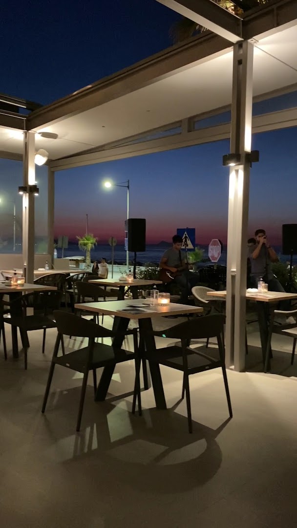Ikones Seafront Luxury Suites vakara pasākums piekrastes terasē ar dzīvo mūziku, galdiņiem un skatu uz saulrietu Retimno