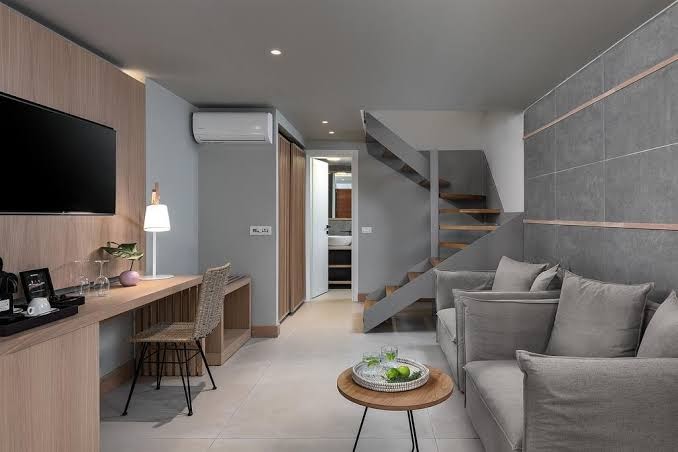 Ikones Seafront Luxury Suites divstāvu numura interjers ar pelēku dīvānu, darba zonu un kāpnēm uz otro stāvu