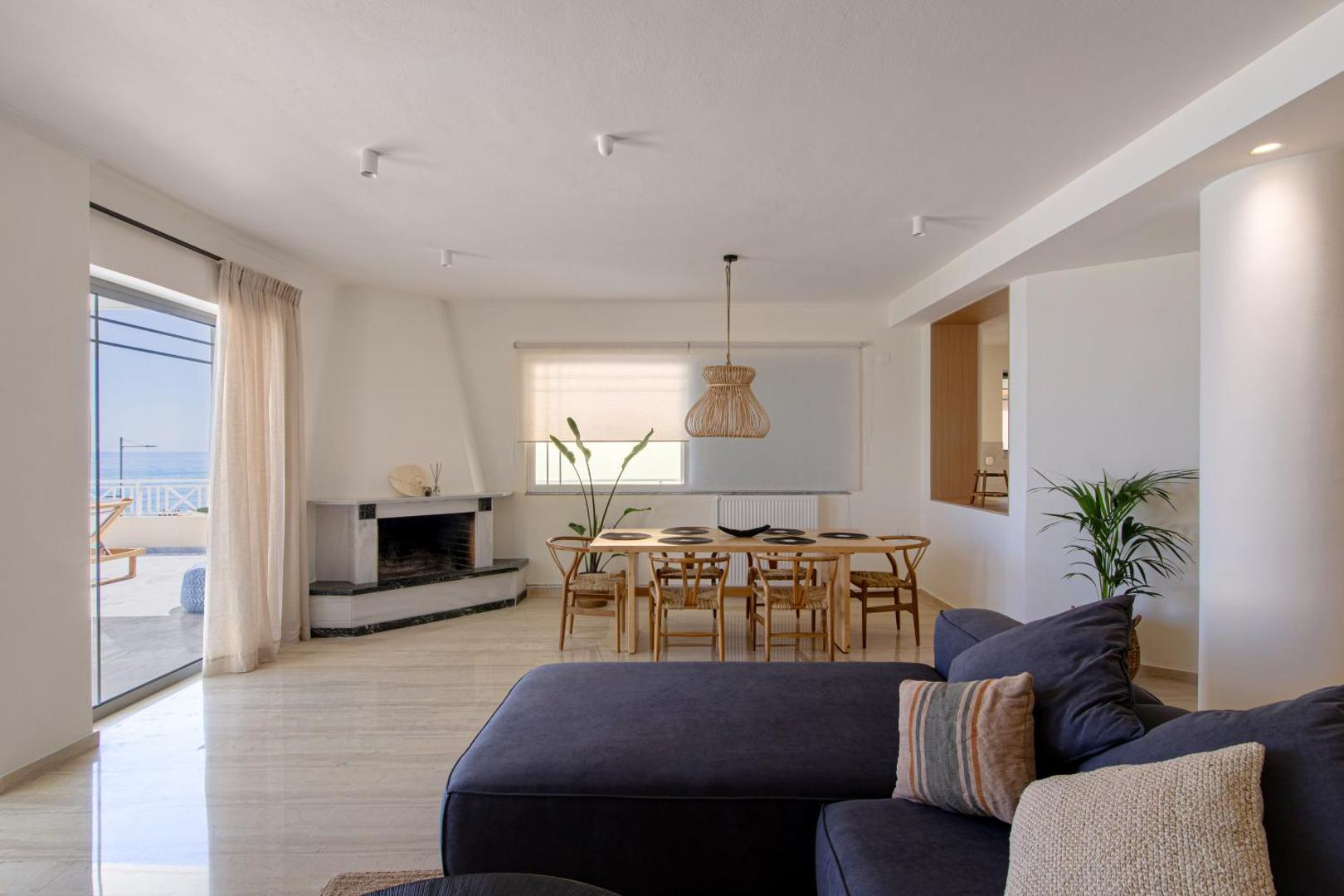Gaišs Ikones Seafront Luxury Suites viesnīcas numurs ar plašu viesistabu, ēdamgaldu, kamīnu un izeju uz balkonu Krētas piekrastē