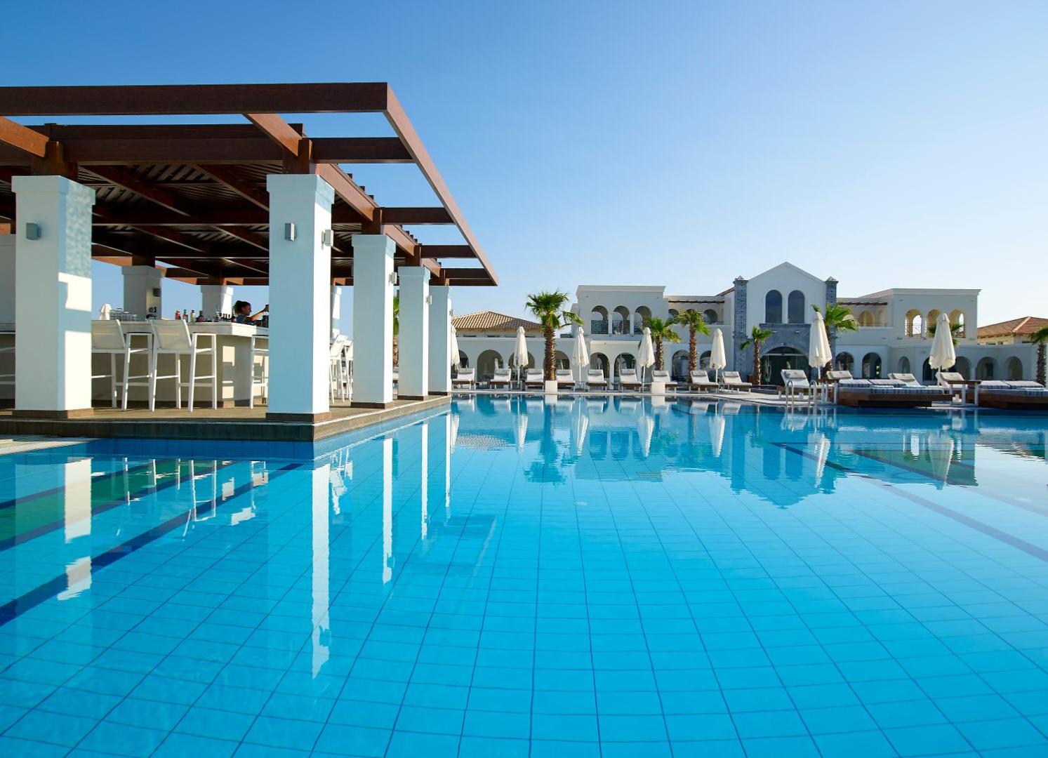 Anemos Luxury Grand Resort āra baseins ar bāru un sauļošanās krēsliem saulainā dienā Georgiupoli, Krētā