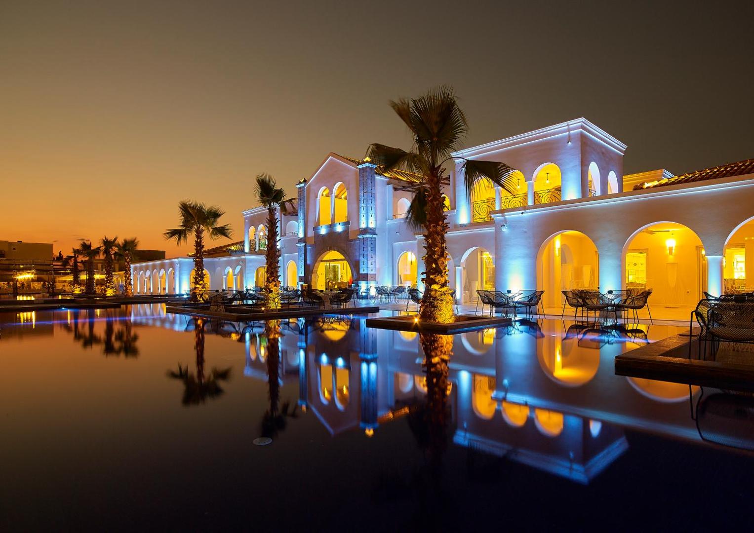 Anemos Luxury Grand Resort galvenā ēka vakarā ar izgaismotām arkām un atspulgu baseinā Georgiupoles reģionā, Krētā