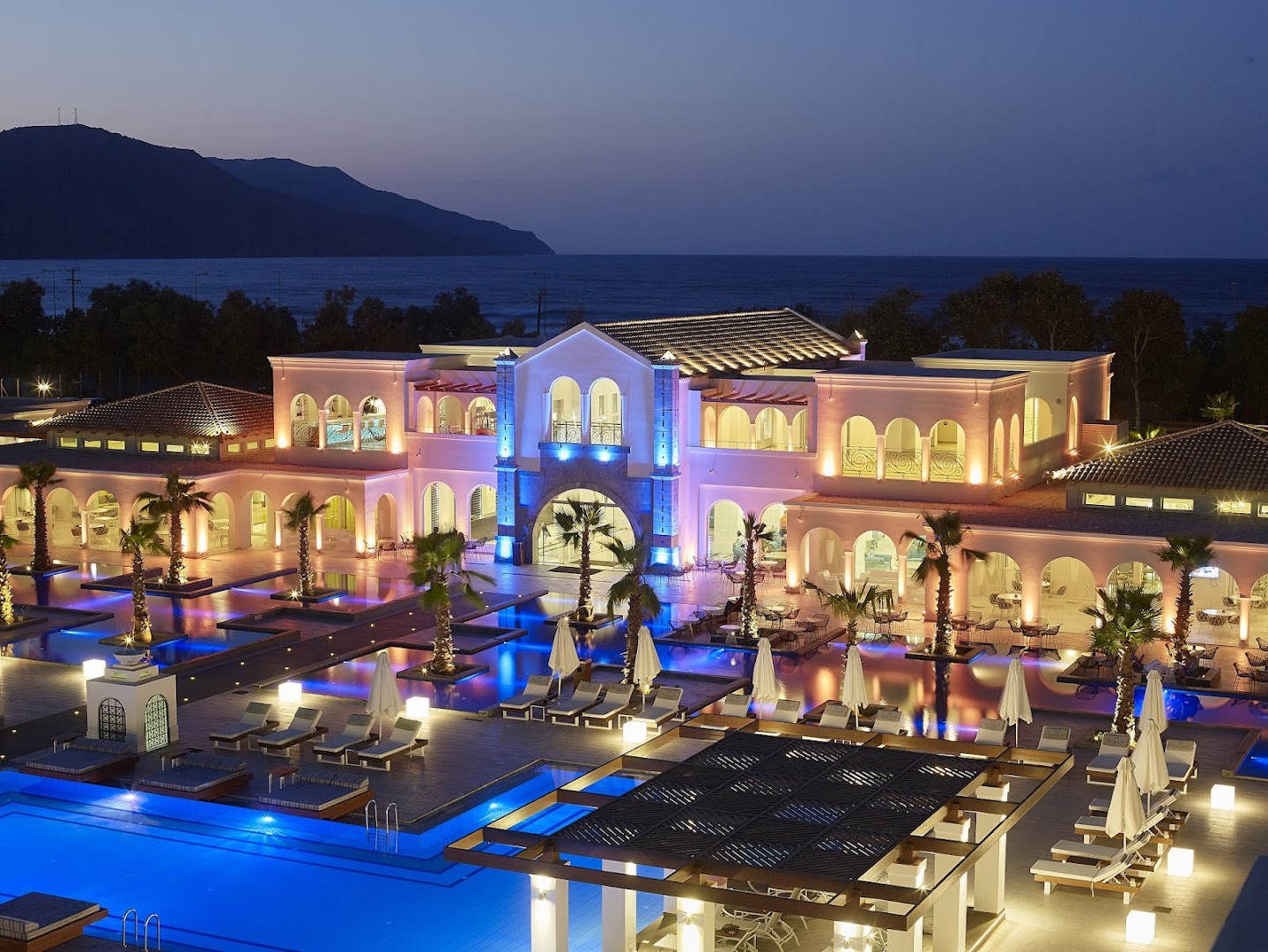 Anemos Luxury Grand Resort nakts skats no augšas uz baseinu kompleksu, sauļošanās terasēm un izgaismoto galveno ēku