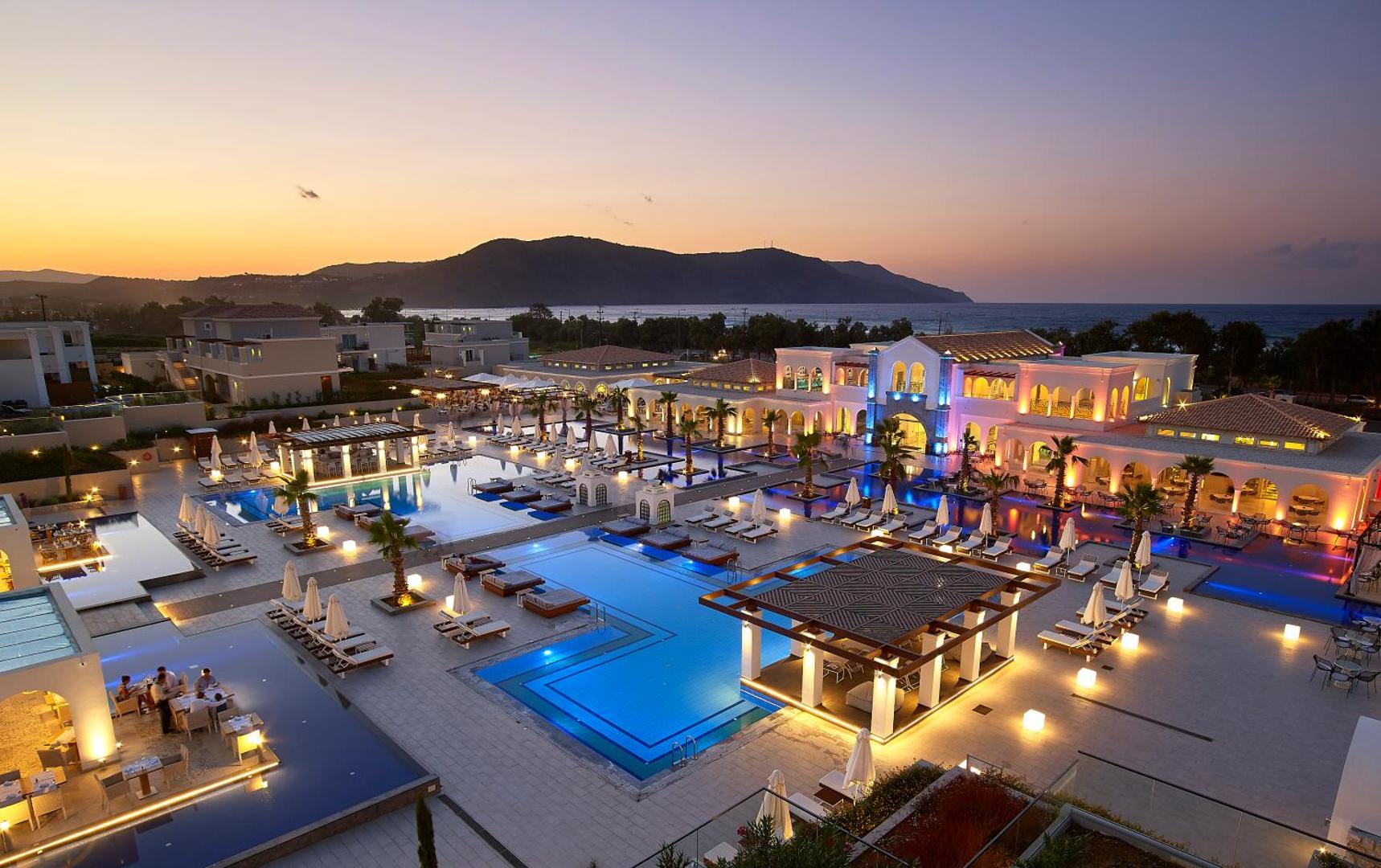 Anemos Luxury Grand Resort vakara panorāma ar izgaismotiem baseiniem, bāru un kalnu fonu Georgiupoli, Krētā