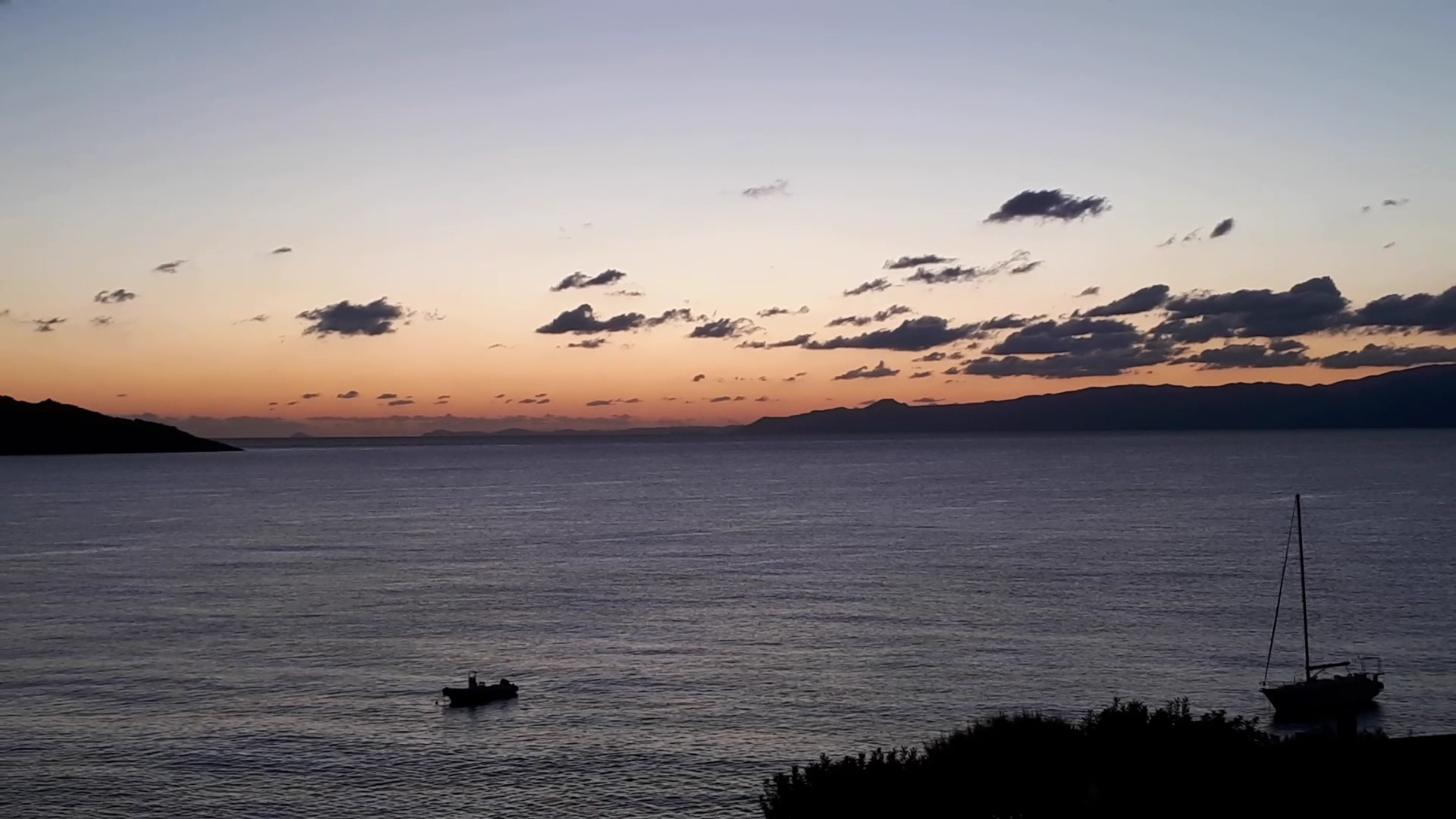 Vakara krēsla pie Elounda Mare Hotel Krētā — jūrā redzamas nelielas laivas un jahtas uz kalnu fona