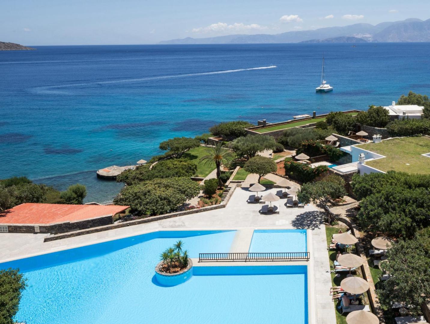 Elounda Mare Hotel plašs galvenais baseins un kūrorta teritorija no augšas ar skatu uz tirkīzzilo jūru un jahtu
