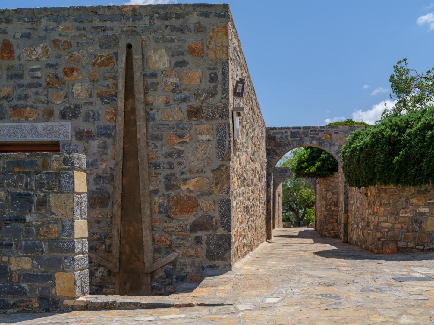 Elounda Mare Hotel tradicionālā akmens arhitektūra ar arkām un bruģētiem celiņiem dārza teritorijā