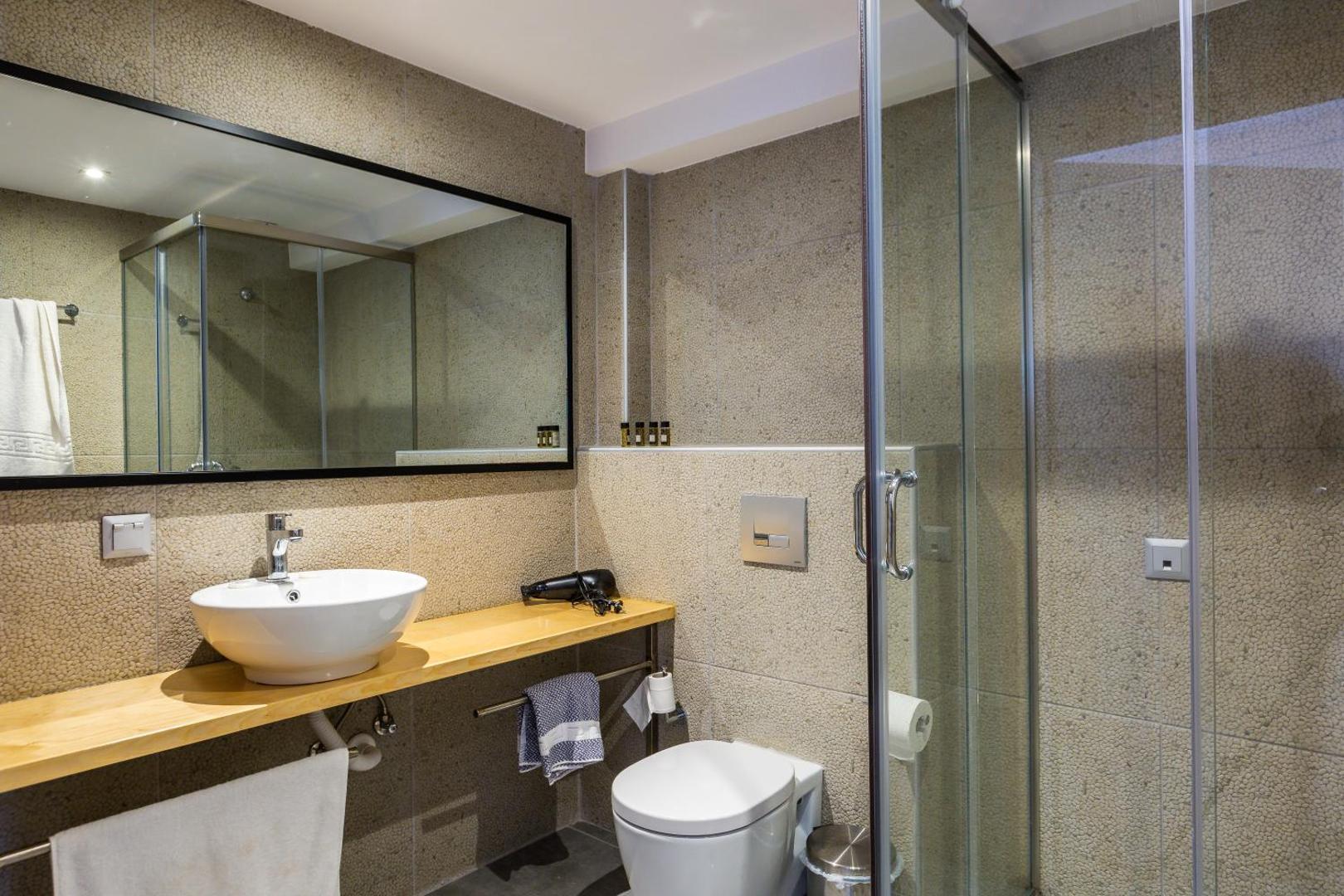 T Hotel Premium Suites numura vannas istaba ar stikla dušas kabīni, lielu spoguli un akmens faktūras sienām
