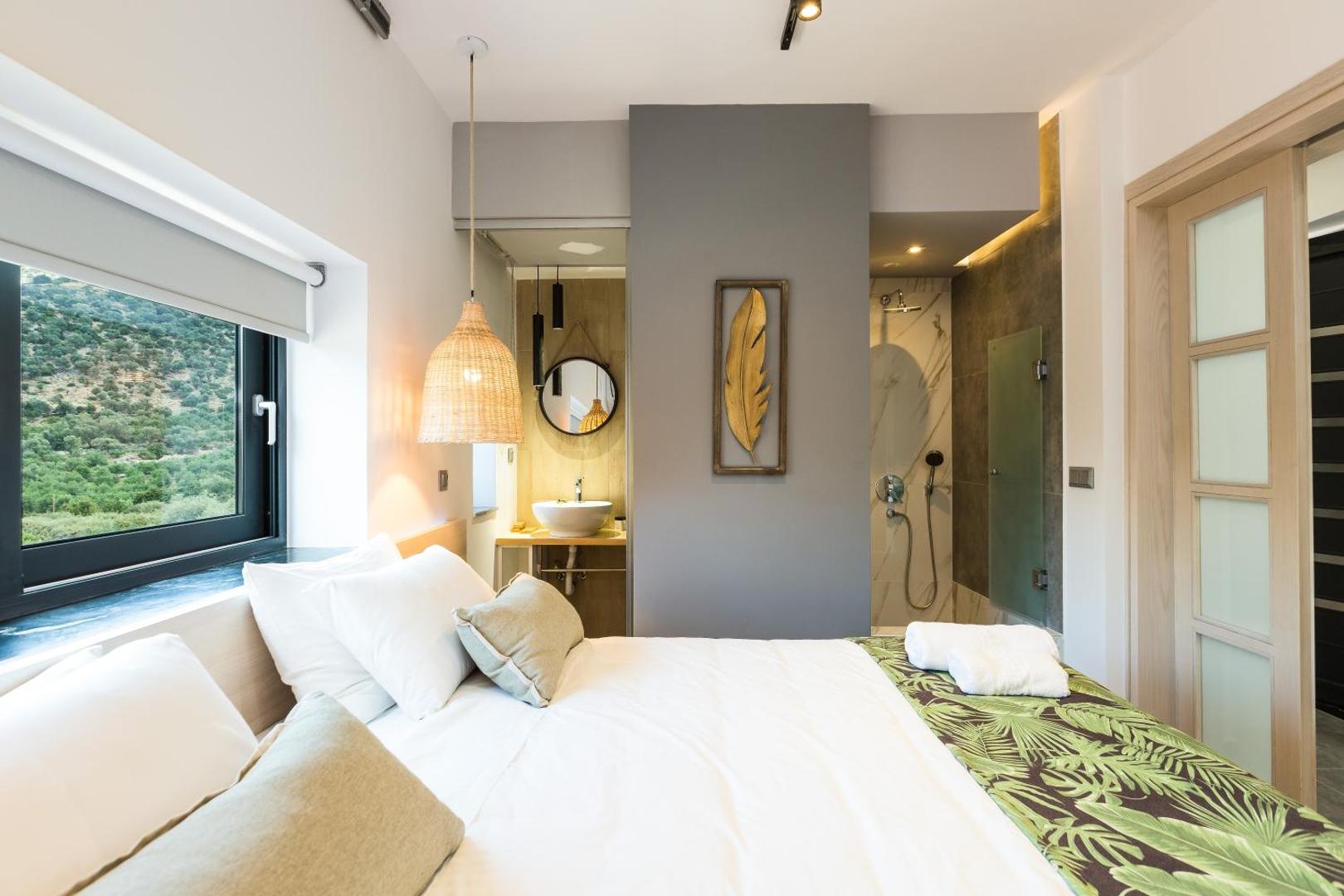 T Hotel Premium Suites moderns numurs ar gaišu interjeru, lielu gultu un atvērta plānojuma vannas istabu ar dušu