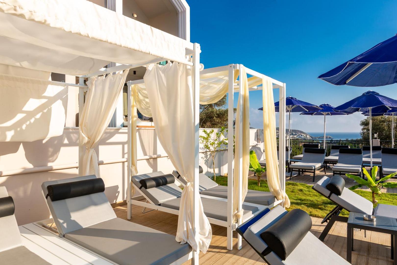 T Hotel Premium Suites atpūtas zona ar baltām nojumēm, ērtiem zviļņiem un skatu uz jūru un kalniem tālumā