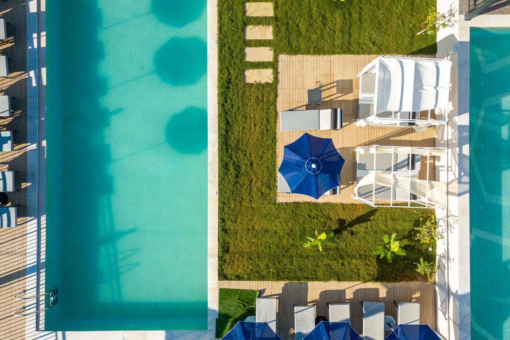 T Hotel Premium Suites skats no augšas uz tirkīzzilu baseinu, koptu zālienu un atpūtas zonu ar saulessargiem un gultām