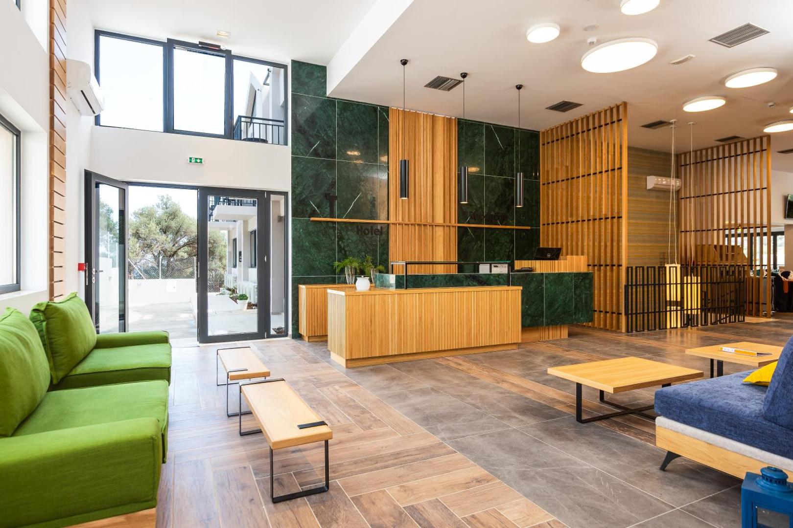 T Hotel Premium Suites plašais vestibils ar modernām mēbelēm, koka apdari un zaļā marmora sienu — skats uz recepciju