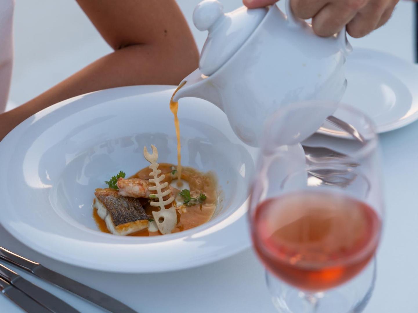 Gourmet vakariņas Caramel Grecotel Boutique Resort restorānā ar zivju ēdienu un rozā vīna glāzi