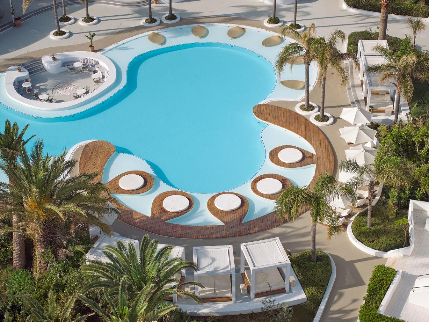 Caramel Grecotel Resort galvenais baseins no putna lidojuma Retimno, Krētā — unikālas formas dizains ar koka platformām un palmām