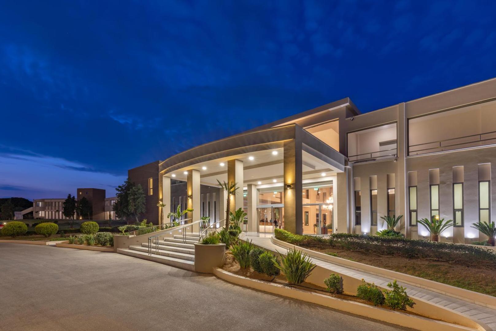 Kresten Royal Euphoria Resort modernā fasāde un piebraucamais ceļš vakarā — izgaismota arhitektūra un palmas pie galvenās ieejas