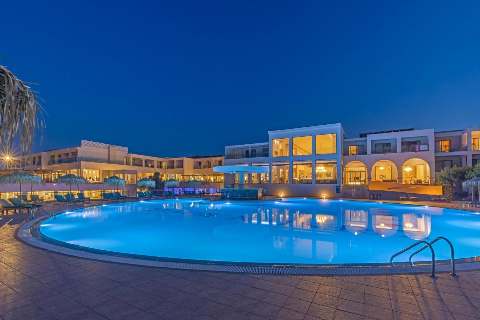 Kresten Royal Euphoria Resort viesnīcas ēka un izgaismots baseins vakarā Rodā — moderna arhitektūra un mājīgs apgaismojums