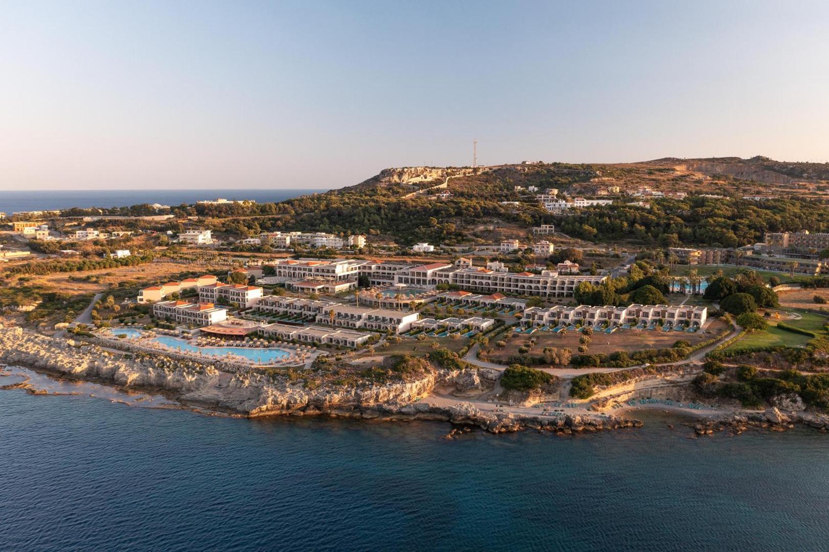 Kresten Royal Euphoria Resort panorāmas skats no putna lidojuma Rodas piekrastē — viesnīcas komplekss, baseini un Vidusjūra saulrietā