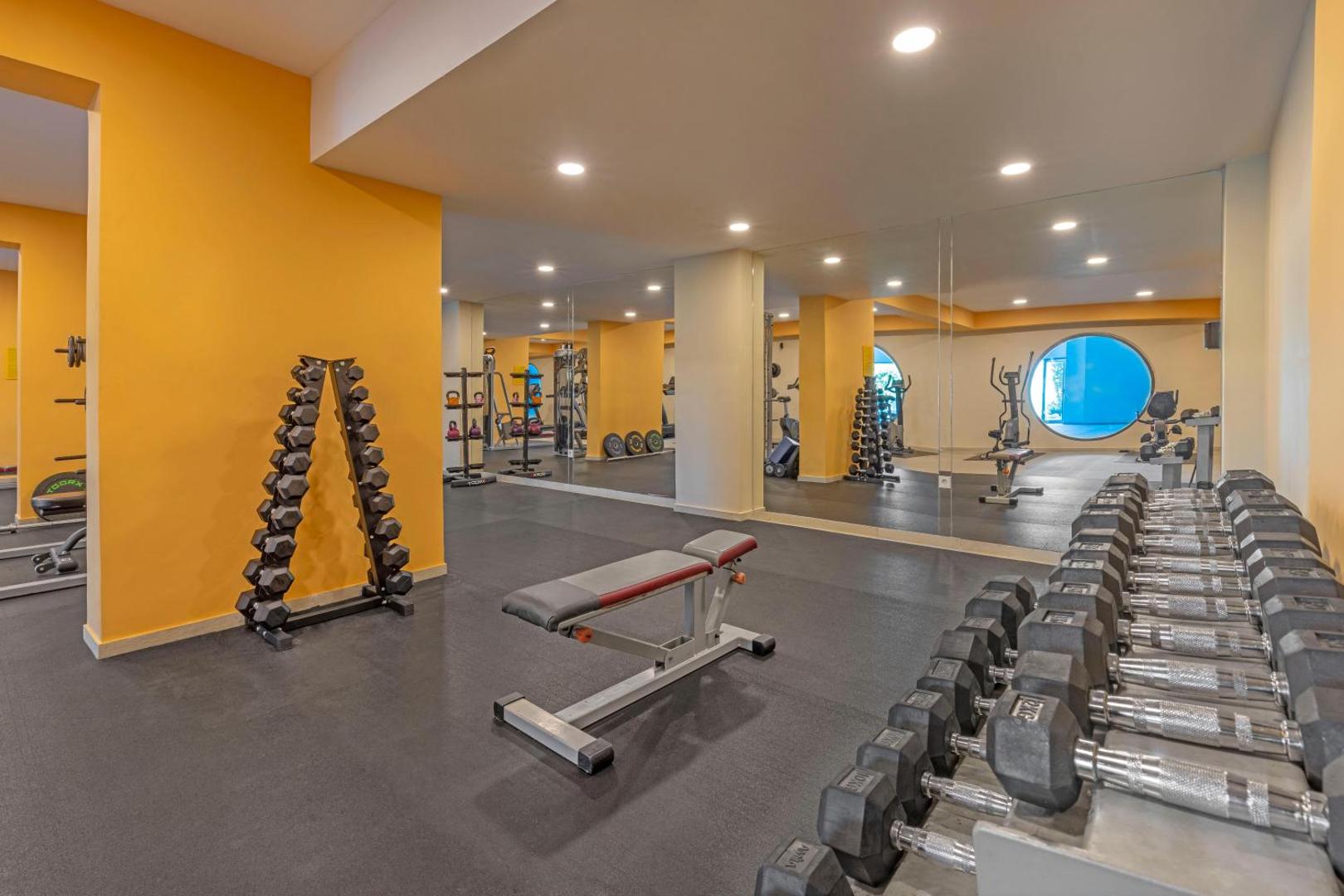 Kresten Royal Euphoria Resort fitness centrs ar plašu hanteļu klāstu, soliem un spoguļu sienām sportiskām aktivitātēm.