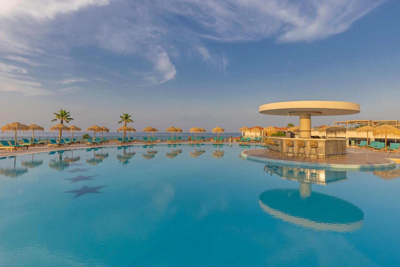 Kresten Royal Euphoria Resort galvenais āra baseins ar bāru ūdenī Rodas piekrastē — saulessargi un atpūtas zona saulrieta gaismā