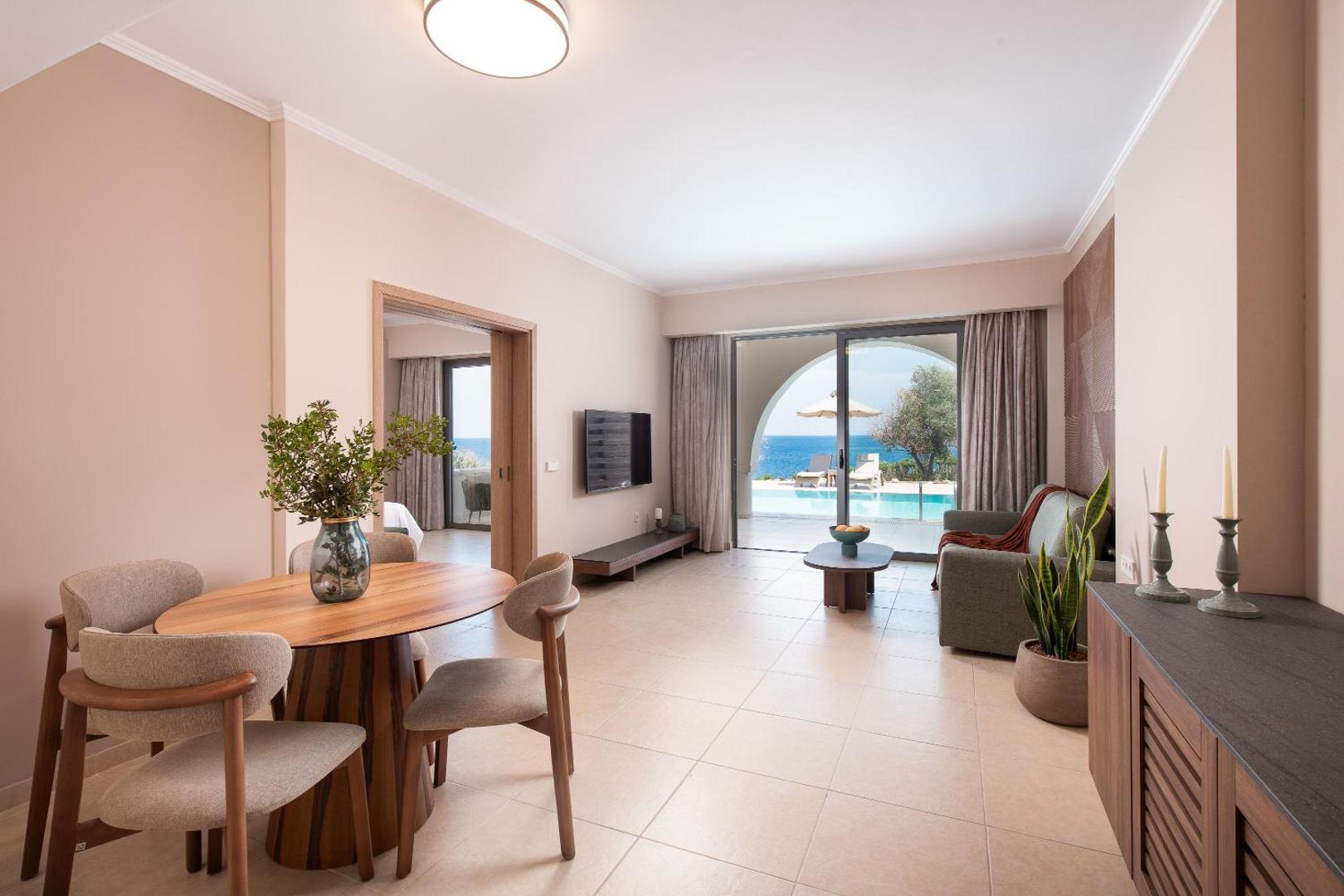 Kresten Royal Euphoria Resort viesistabas zona ar ēdamgaldu, dīvānu un izeju uz terasi ar skatu uz jūru Rodā.