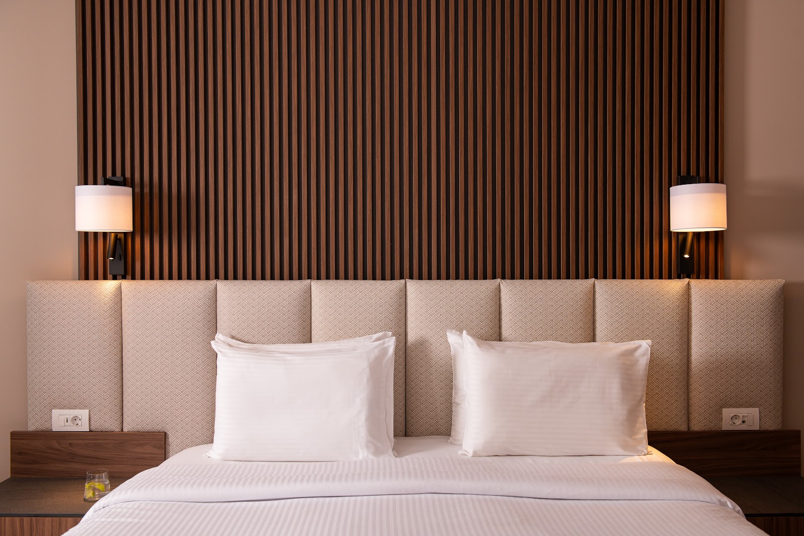 Kresten Royal Euphoria Resort numura interjera detaļa — gultas galvgalis ar koka apdari un modernu apgaismojumu.