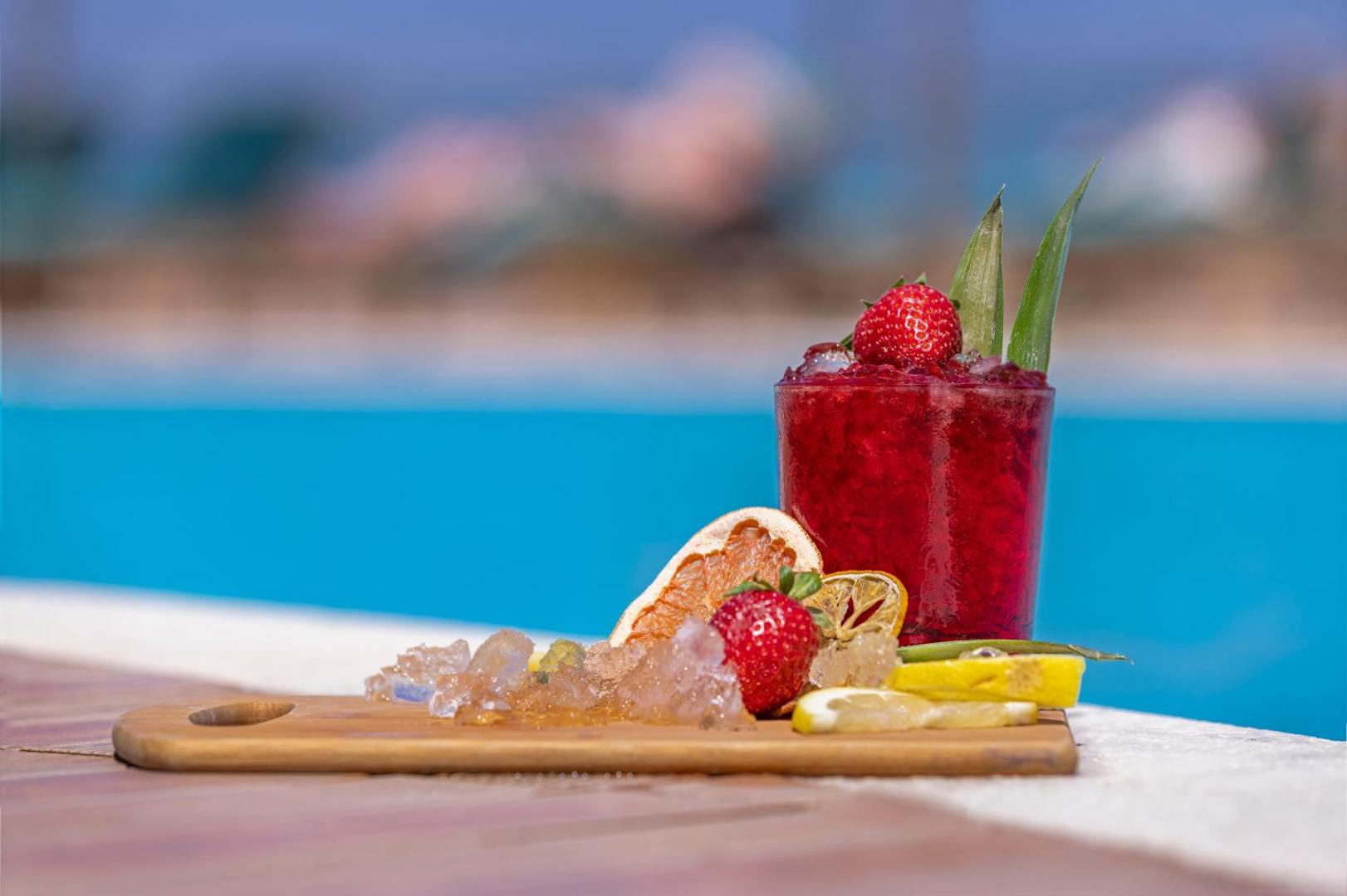 Sarkans ogu kokteilis ar zemenēm un ledu uz koka dēlīša pie Kresten Royal Euphoria Resort baseina Rodā.