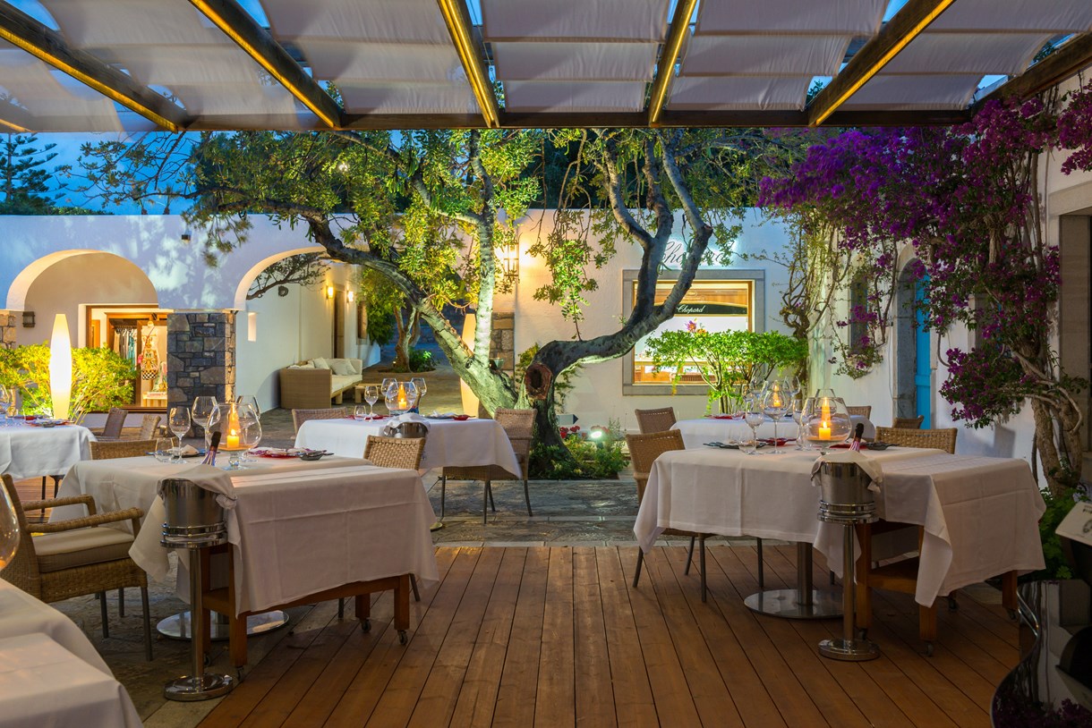 Elounda Beach Hotel And Villas vakariņu zona brīvā dabā ar svecēm uz galdiem un ziedošām bugenvillijām vakarā