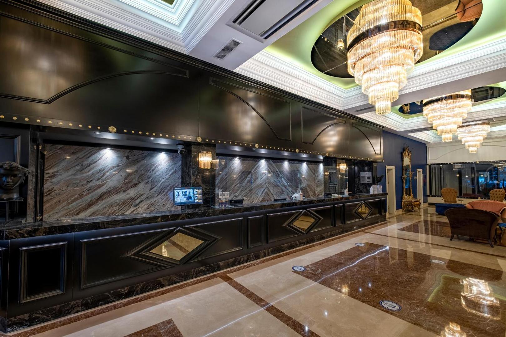 Utopia Resort & Residence viesnīcas recepcijas zona ar greznām lustrām, marmora grīdu un tumša koka apdares reģistratūras galdiem Alanjas reģionā