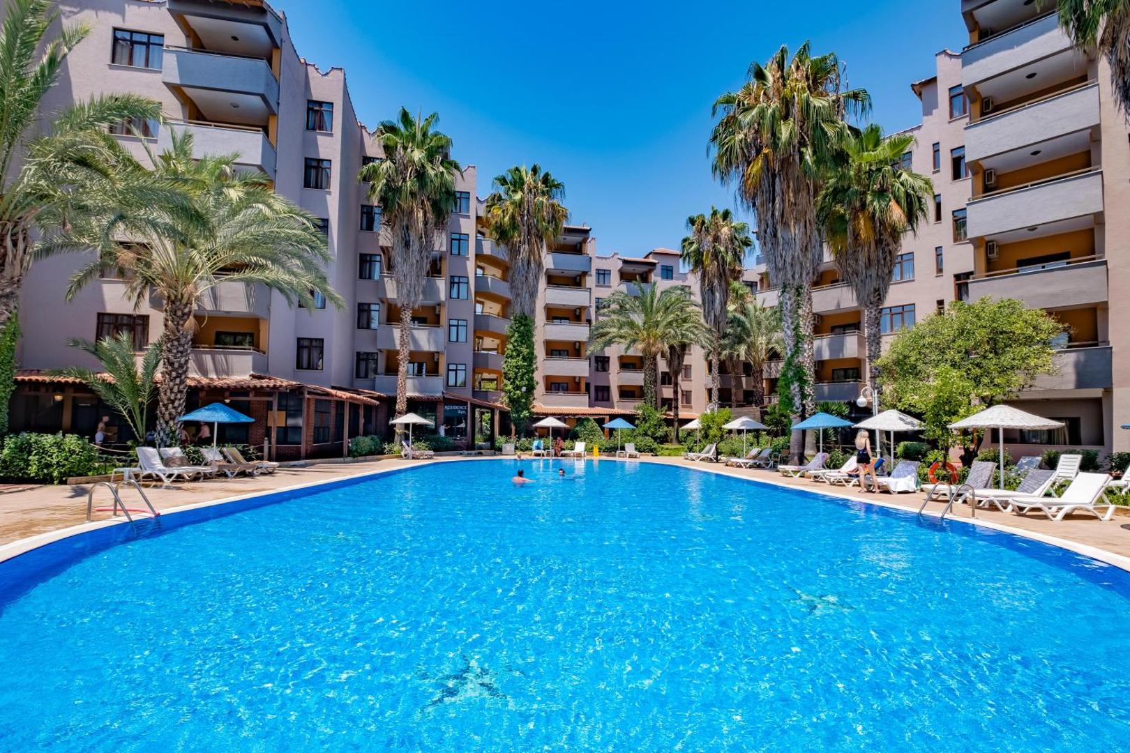 Utopia Resort & Residence iekšpagalma baseins starp viesnīcas korpusiem un augstām palmām — sauļošanās krēsli un saulains laiks