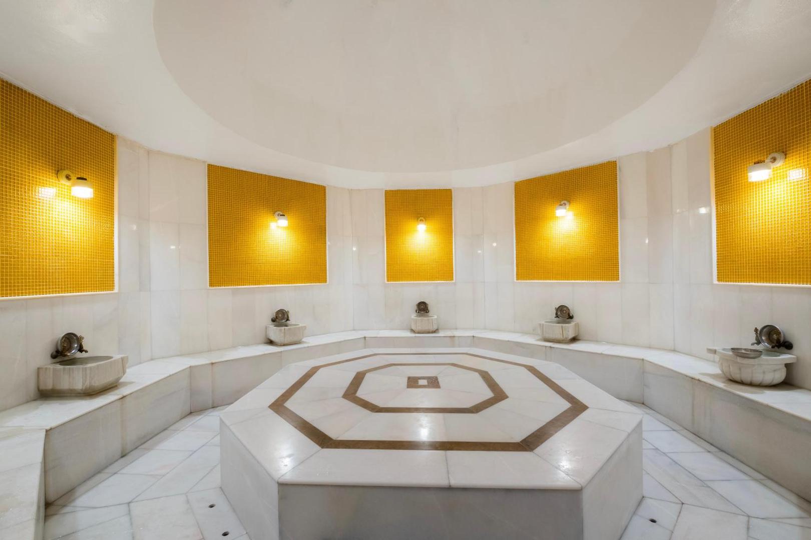 Tradicionāls turku hamams Utopia Resort & Residence spa centrā ar marmora apdari, centrālo akmens platformu un dekoratīvām dzeltenām flīzēm