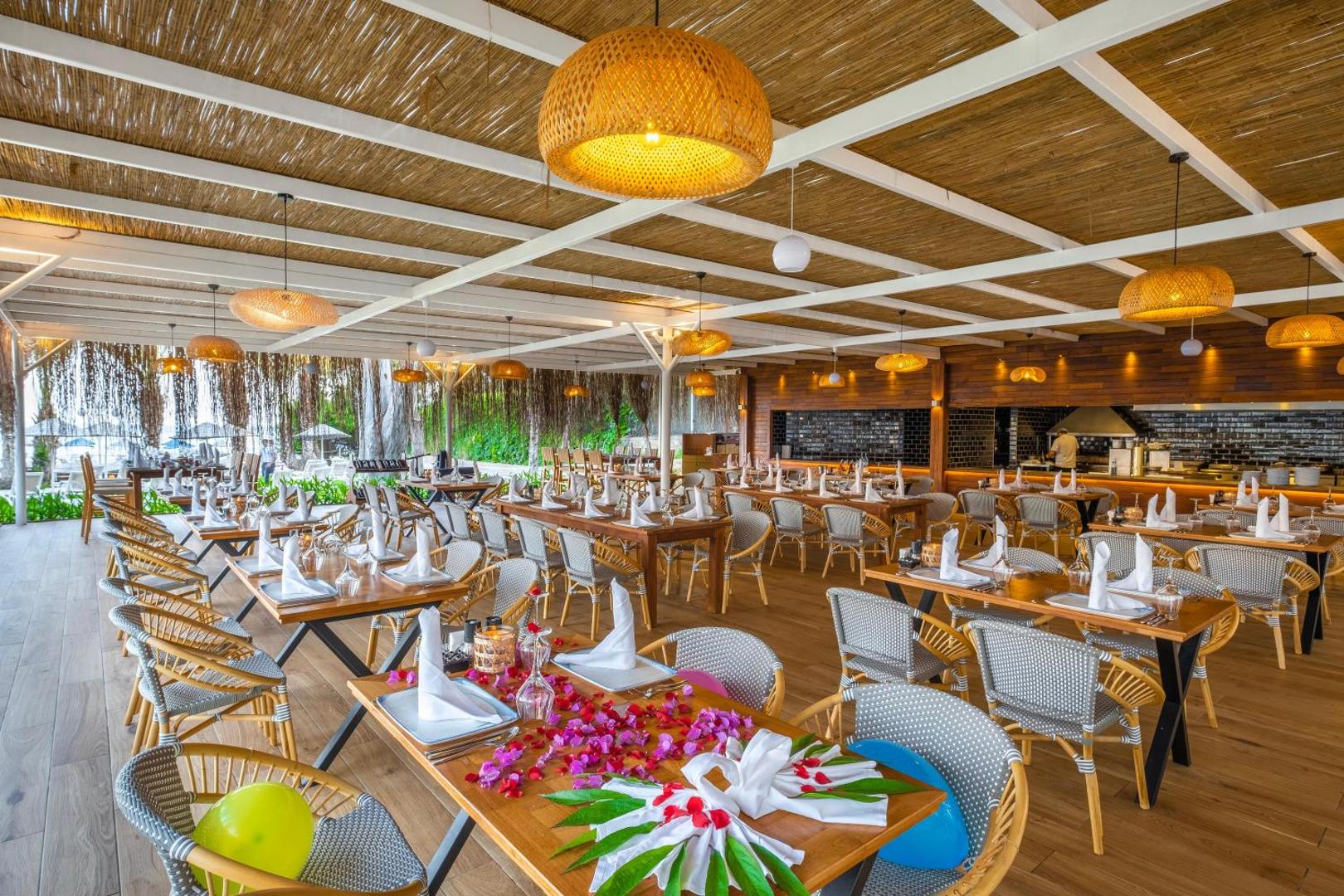 Utopia Resort & Residence pludmales restorāns ar koka apdari, pītiem gaismekļiem un svētku galda klājumu Turcijas kūrortā.