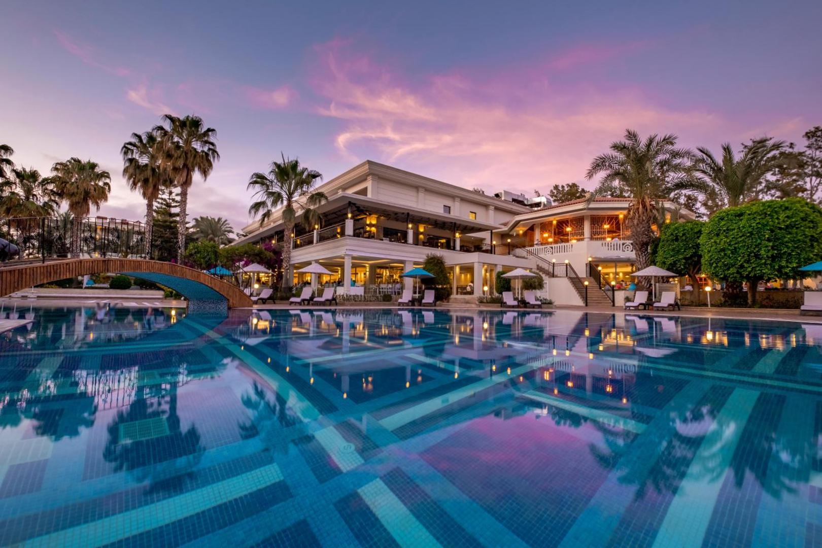 Utopia Resort & Residence galvenais baseins un viesnīcas ēka saulrietā Alanjas reģionā — izgaismota terase, palmas un vakara debesis