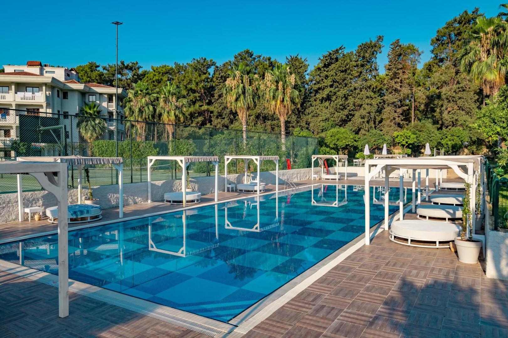 Utopia Resort & Residence baseins ar stilīgām atpūtas gultām un nojūmēm — apkārtnē priežu mežs un tenisa korti